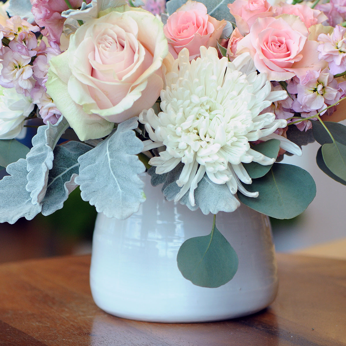 Floral arrangement with pink and white flowers in a white vase on a wooden surface.
