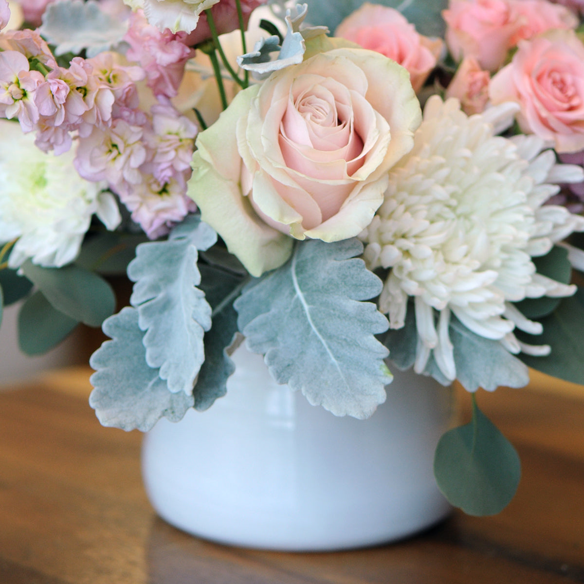 Floral arrangement with pink and white flowers in a white vase on a wooden surface
