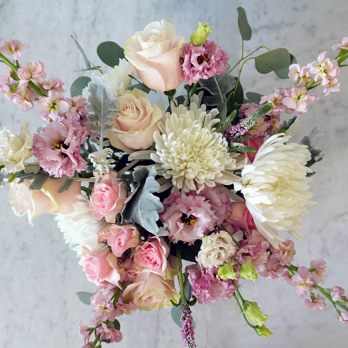 Top down view of Bouquet of pink, white, and green flowers on a light gray background