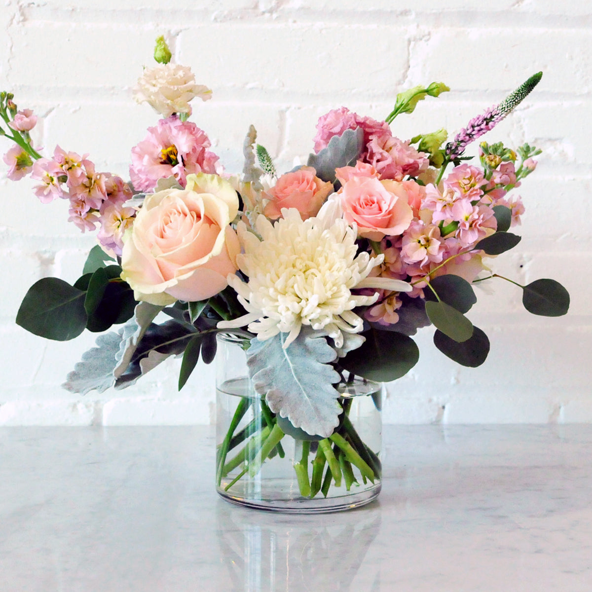 Bouquet of flowers in a clear vase on a white surface with a white brick wall background
