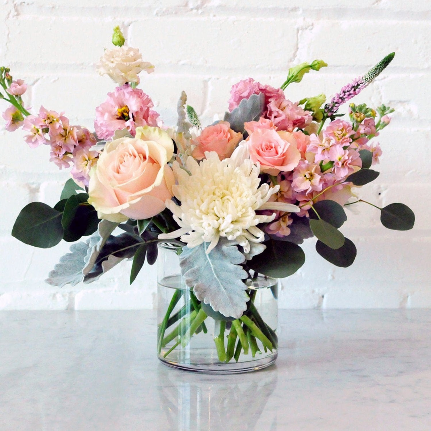 Bouquet of flowers in a clear vase on a white surface with a white brick wall background