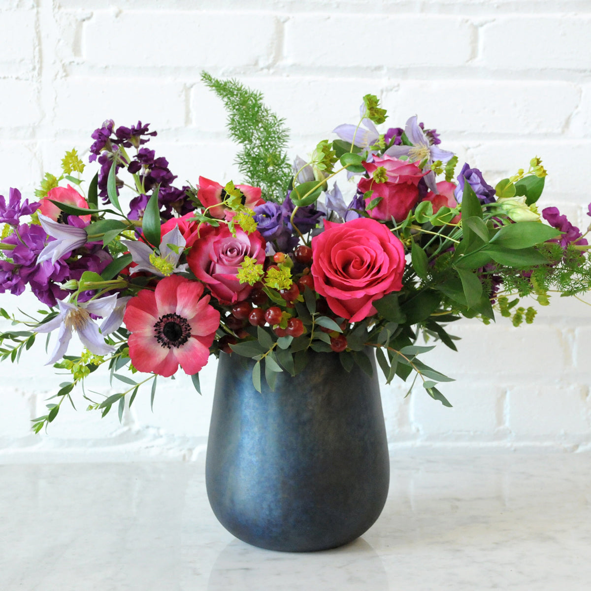 Spruce Floral arrangement in Blue Raindrop vase with Pink and Lilac roses Scented Stock and Anemone