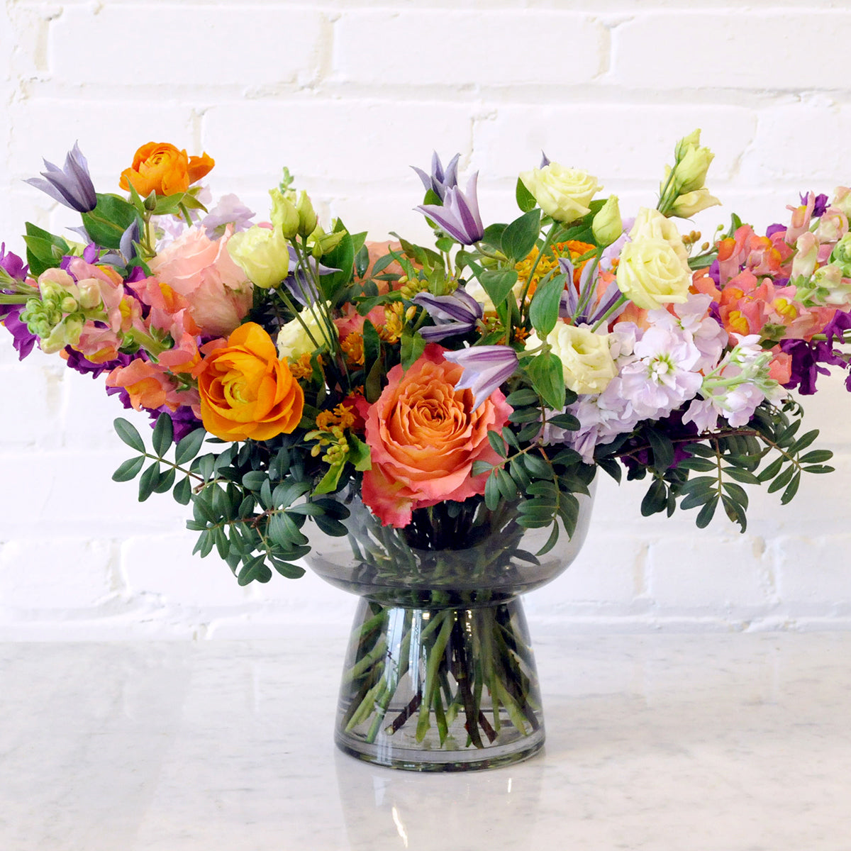 Spruce Flowers Whimsical Channing floral arrangement, Country garden style featuring a high flower count artistically arranged in a smoked glass compote vase