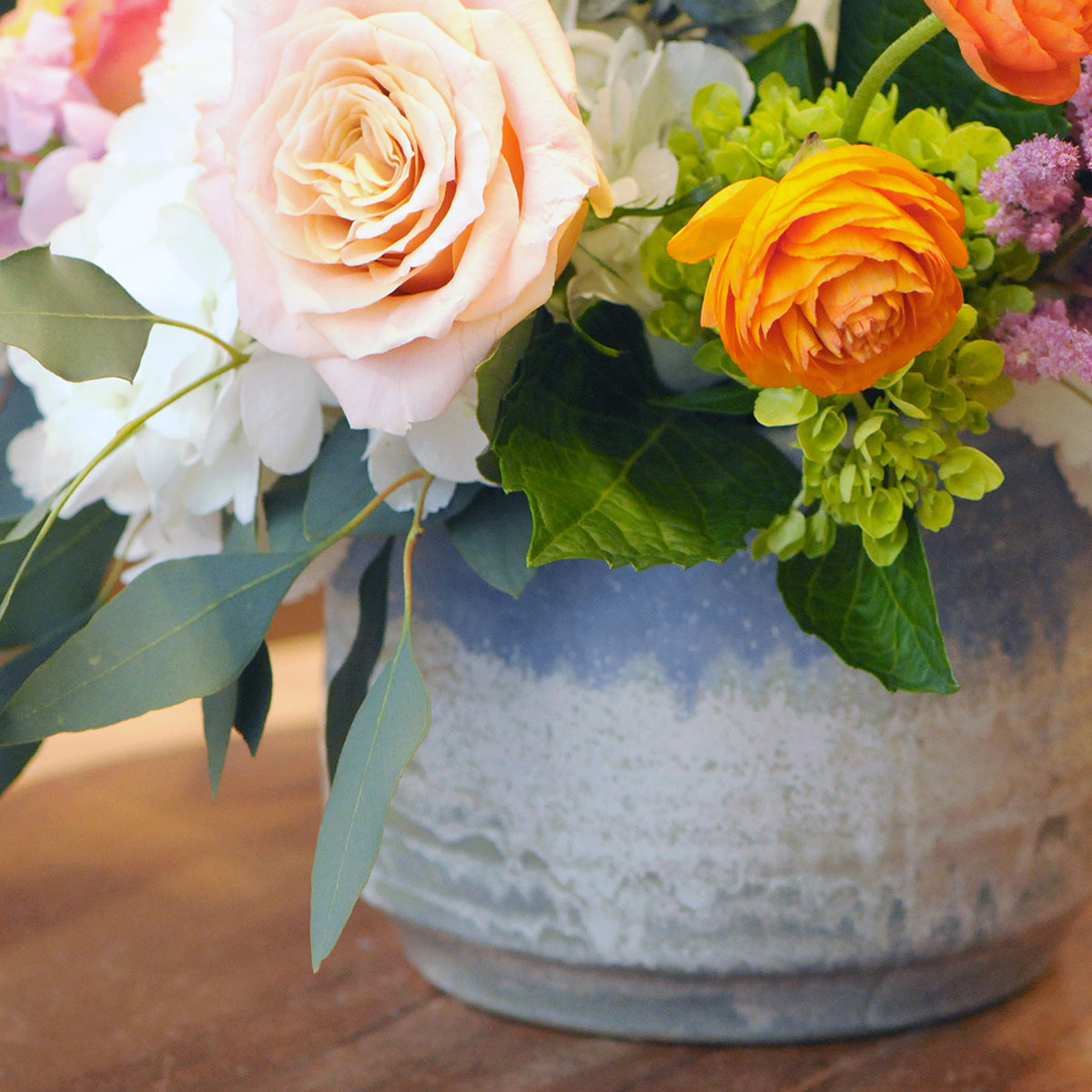 Spruce Flowers floral arrangement in detail showing peach Roses and Ranunculus in a textured ceramic vase