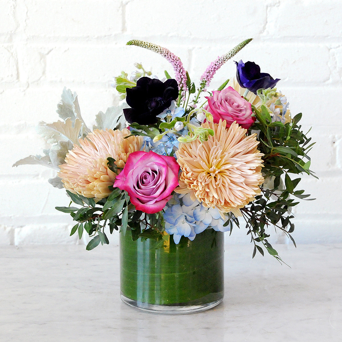 Spruce Flowers glass cylinder vase with a foliage leaf wrap to hide the stems. with Emerson arrangement of Blue Hydrangea and Cremon Chrysanthemums