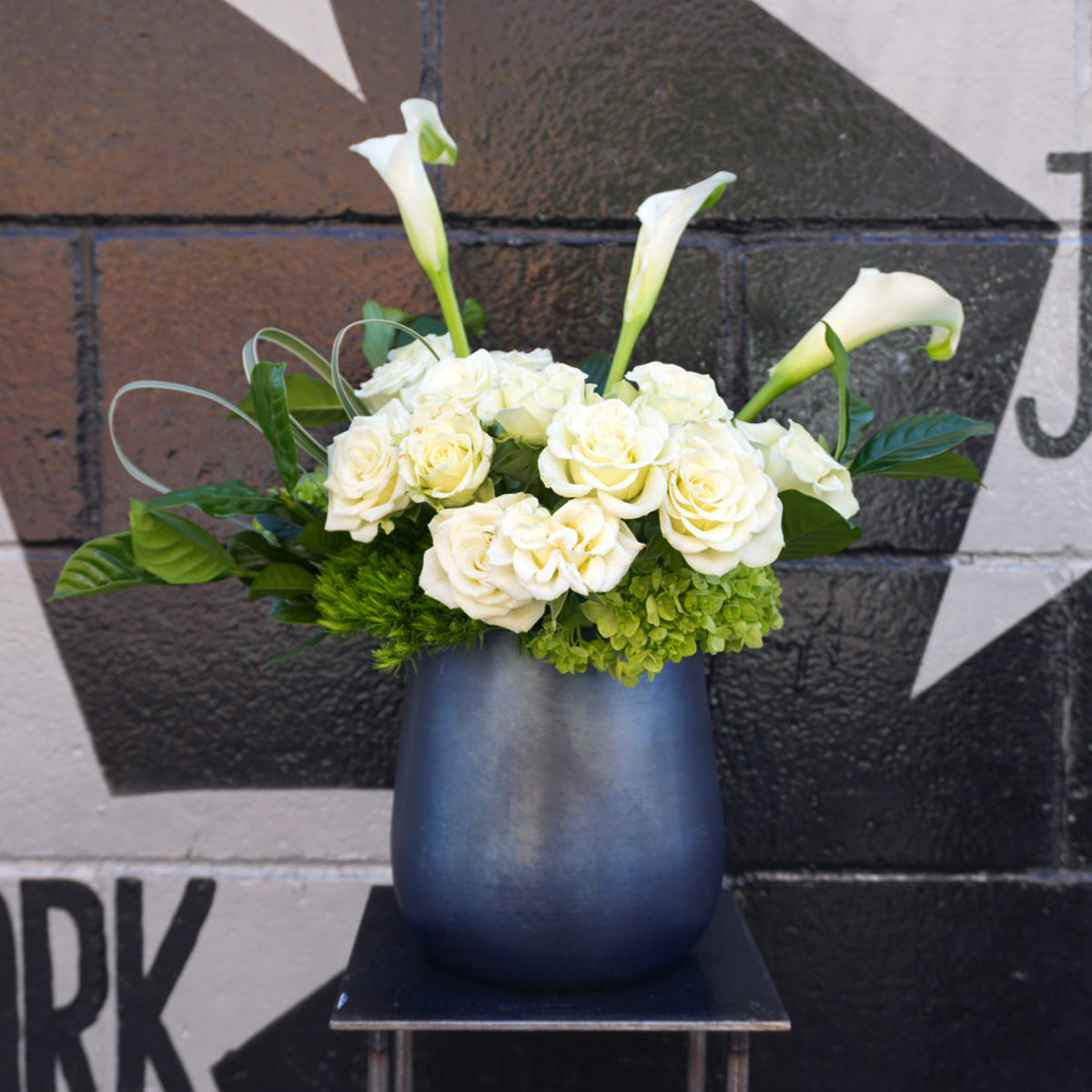 Floral arrangement with white flowers and greenery in a blue vase against a black and white wall.