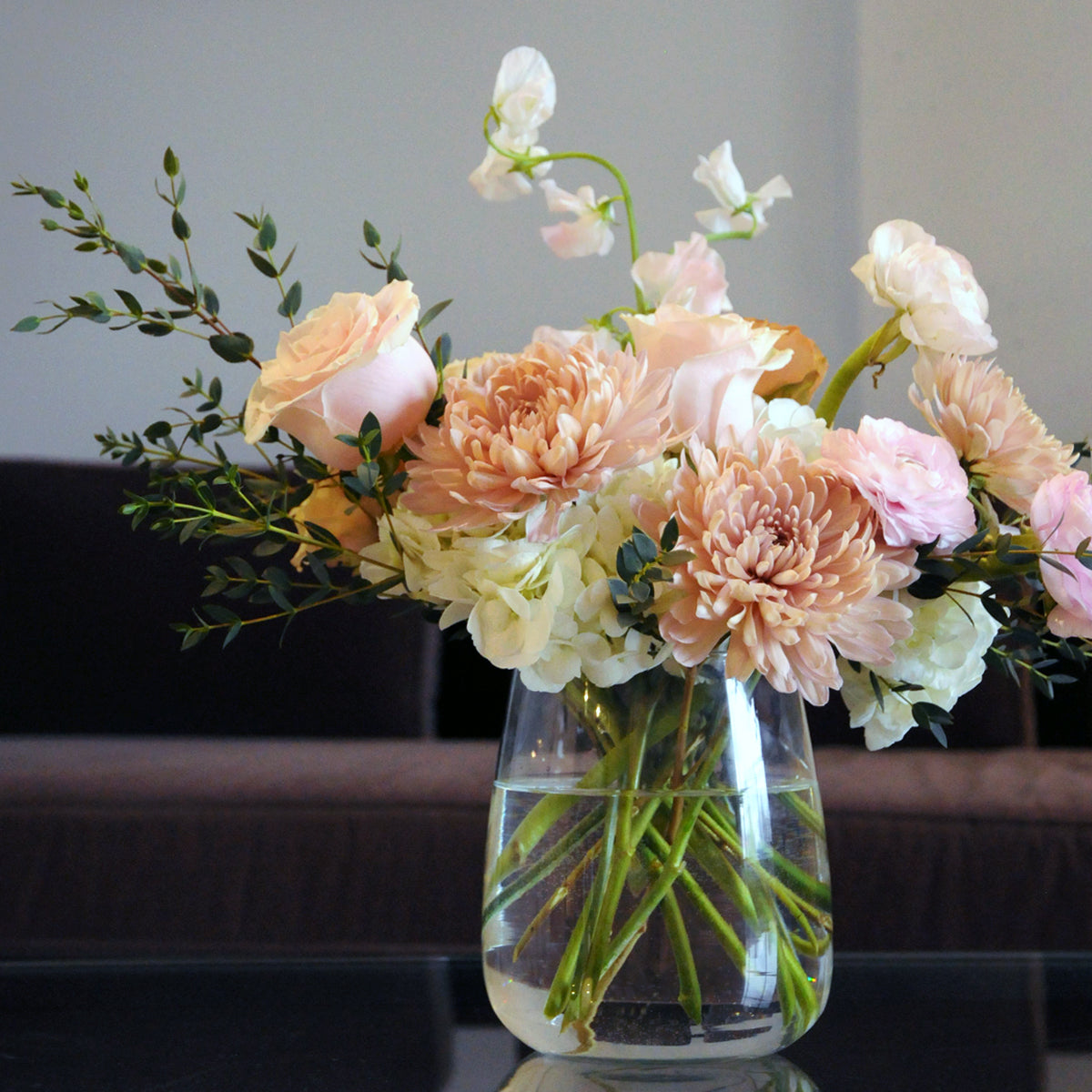 France Avenue arrangement set on a glass table featuring opeach and soft pink florals