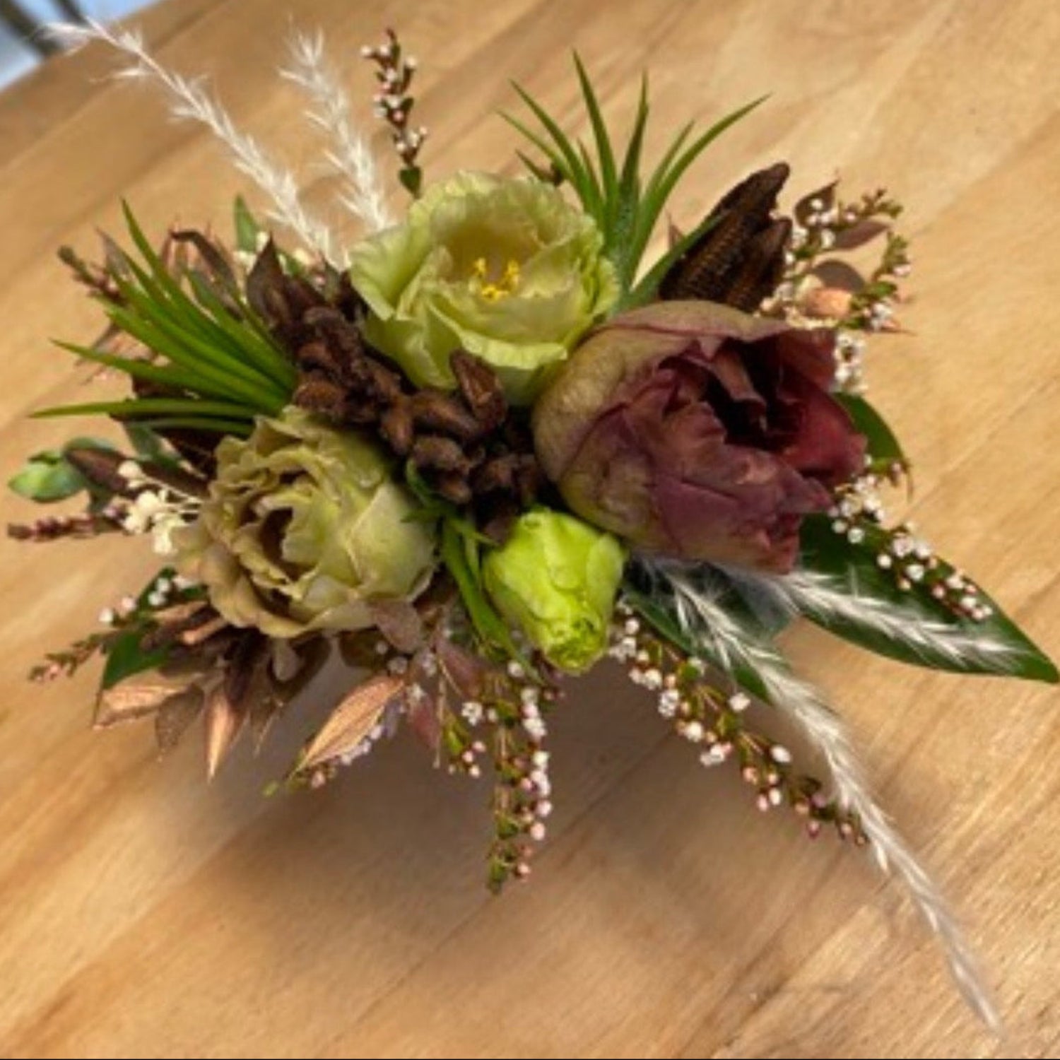 A floral corsage featuring pale green Lisianthus , seed pods, and dried grasses on a light wood background
