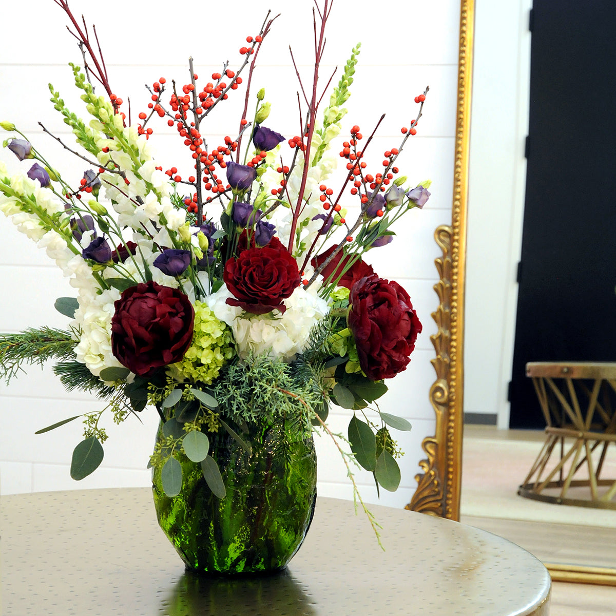 Bouquet of flowers in a green vase on a table with a decorative mirror in the background.