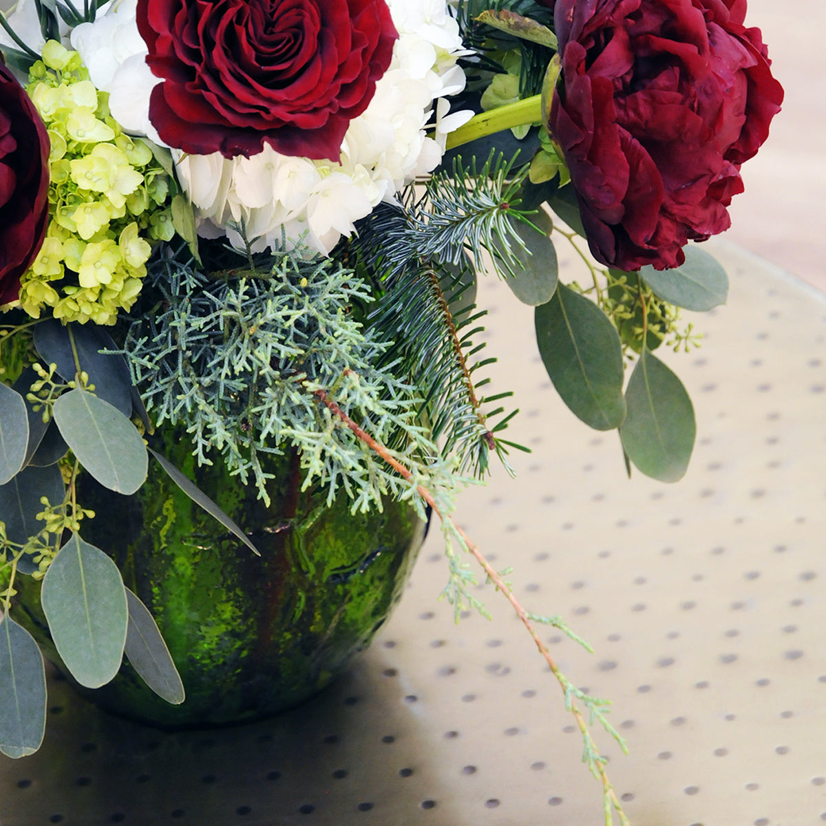 Bouquet of red, white, and green flowers in a decorative container on a patterned surface.