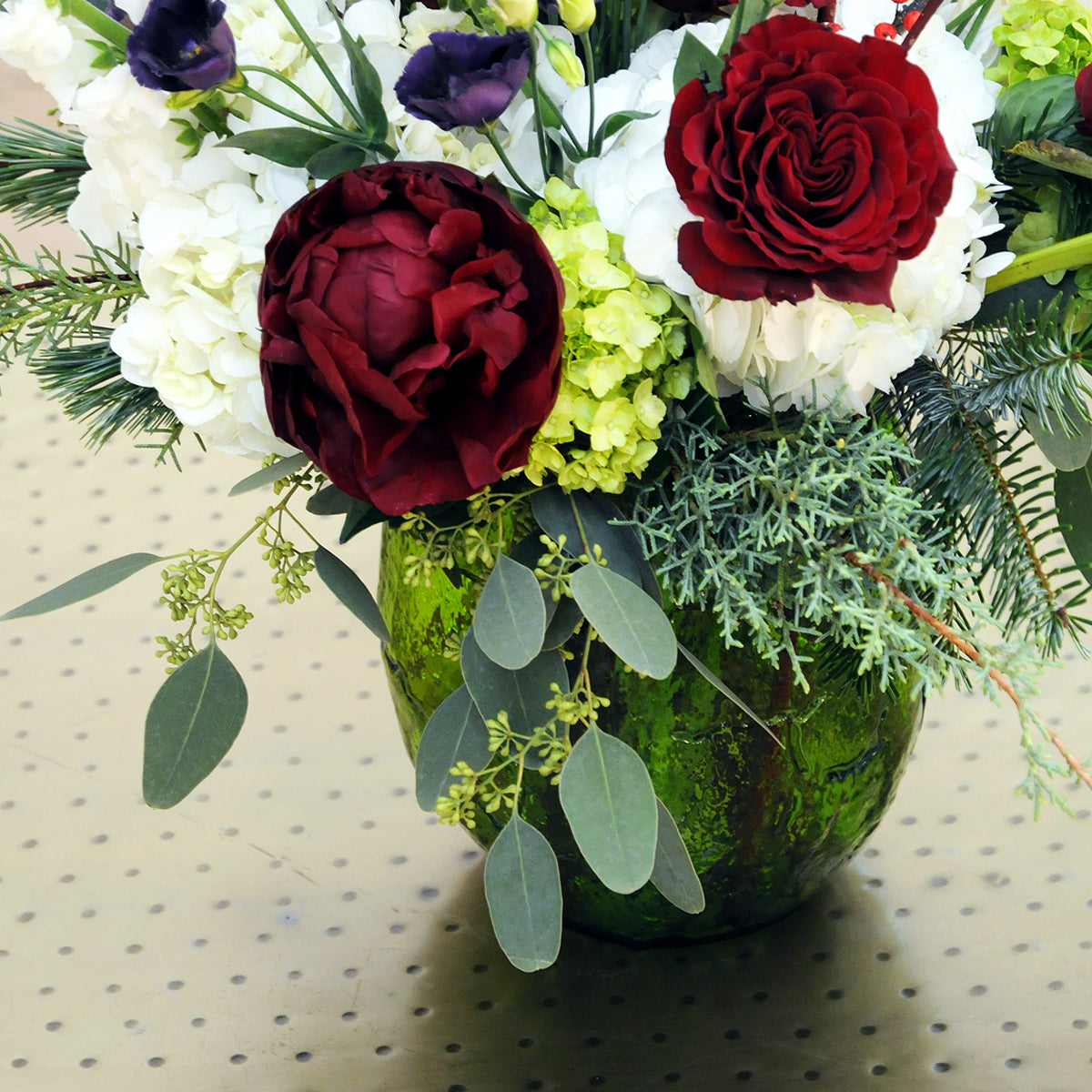 Bouquet of red, white, and purple flowers in a green vase on a polka dot surface