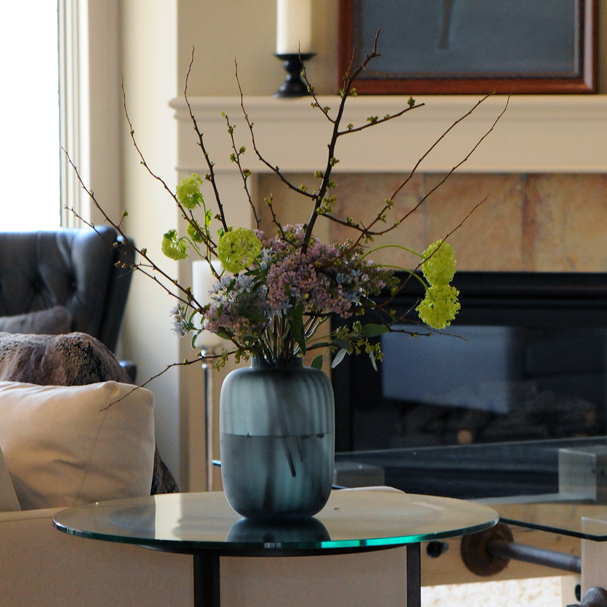 Decorative vase with flowers on a glass table in a living room setting.