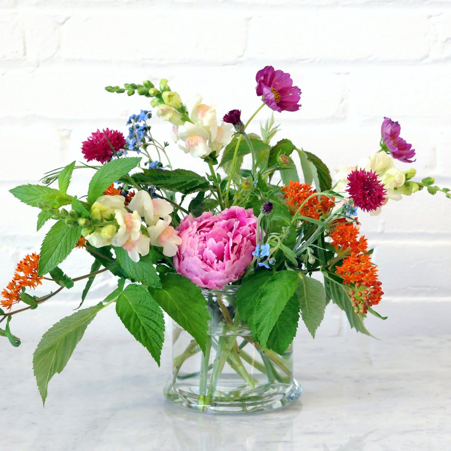 An example of the Larpenteur arrangement featuring peonies and asclepius shown in a glass cylinder