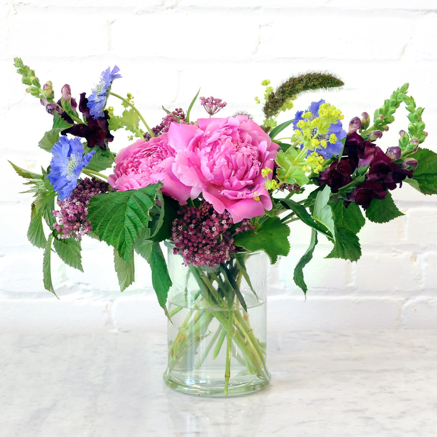 An example of the Larpenteur arrangement featuring peonies shown in a tall glass cylinder