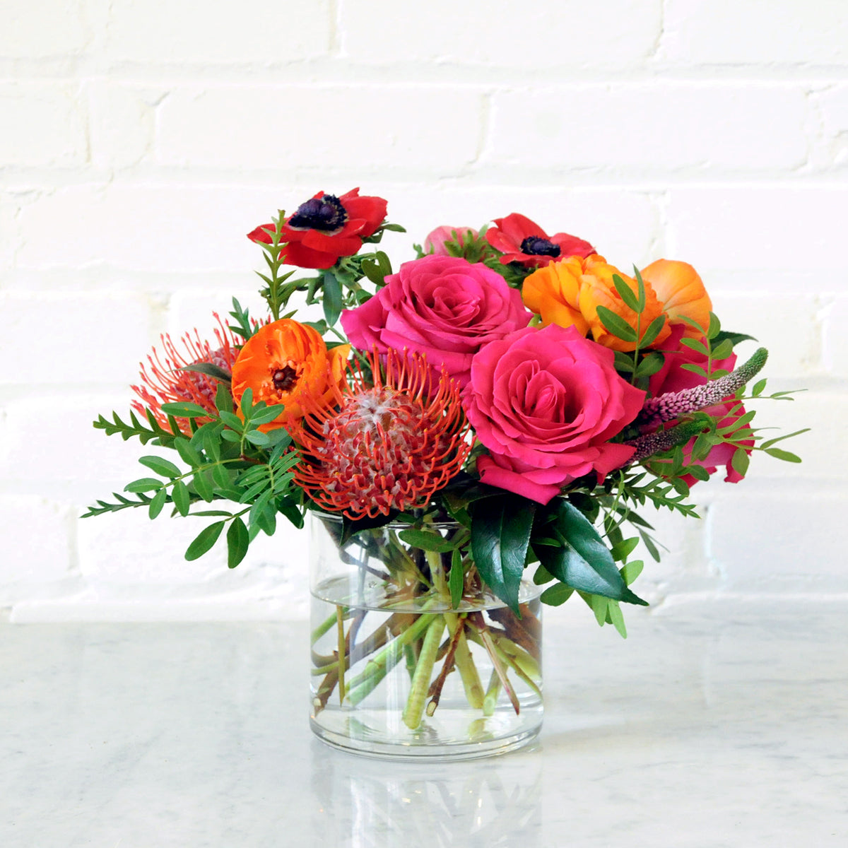 The Lexington Floral arrangement with Red Protea Pink Roses and Pistachio foliage in a glass Vase