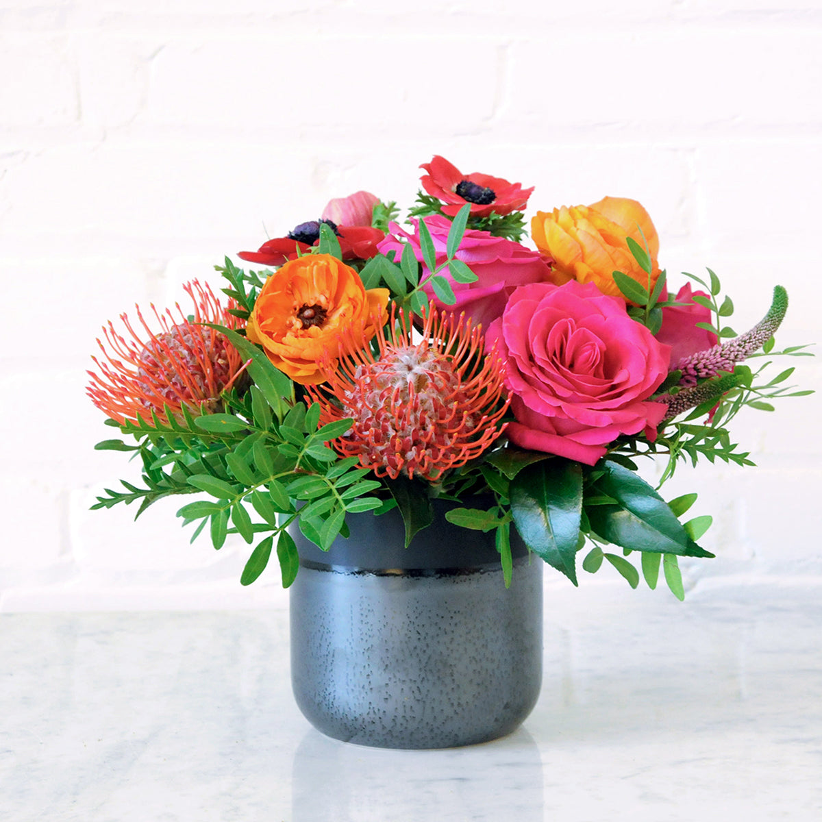 The Lexington Floral arrangement Modern in Styling with grouped Pink Floyd Roses , Ranuculus and Anemone in our Lennon Black ceramic vase