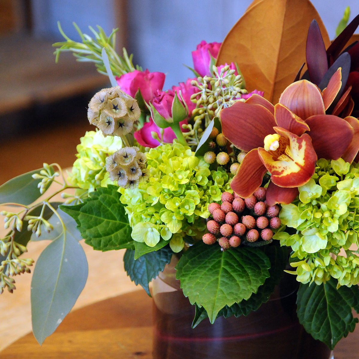 Colorful flower arrangement with green hydrangeas, pink roses, and red orchids on a wooden surface.