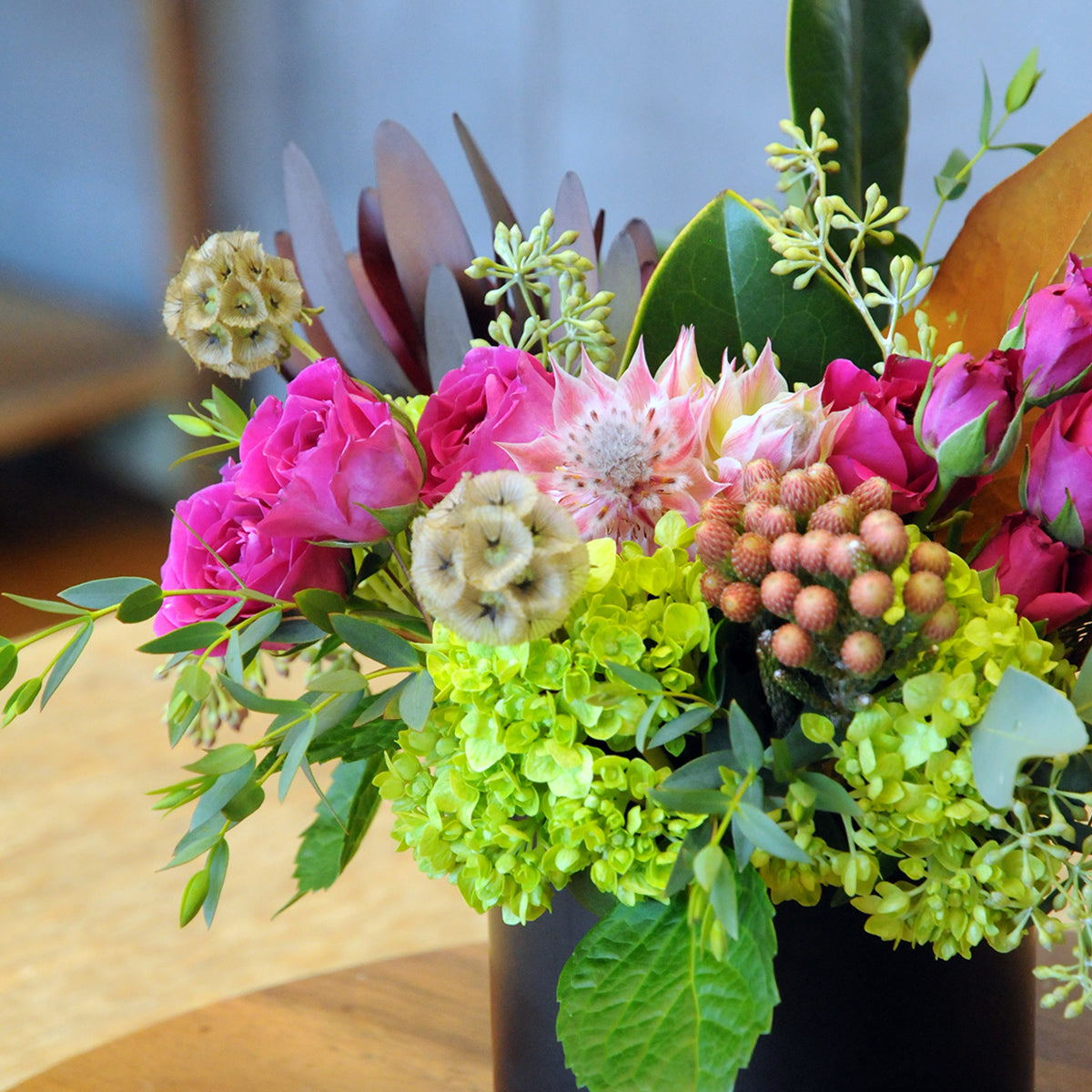 Colorful flower arrangement with pink, green, and purple flowers on a wooden surface.