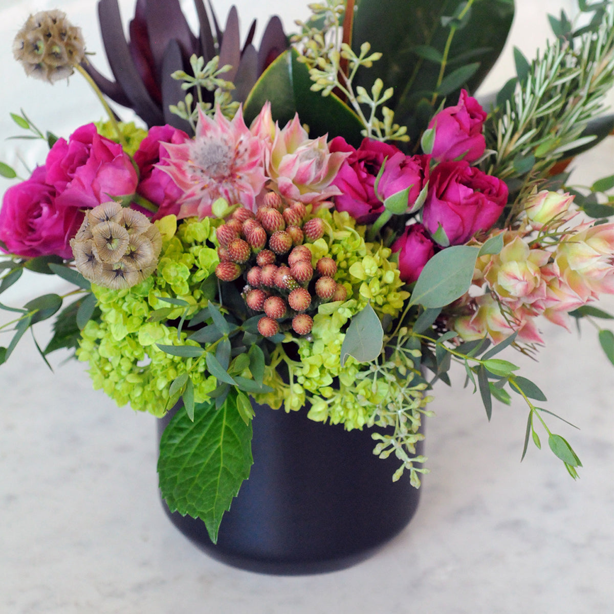 Floral arrangement with pink and green flowers in a black vase on a light background