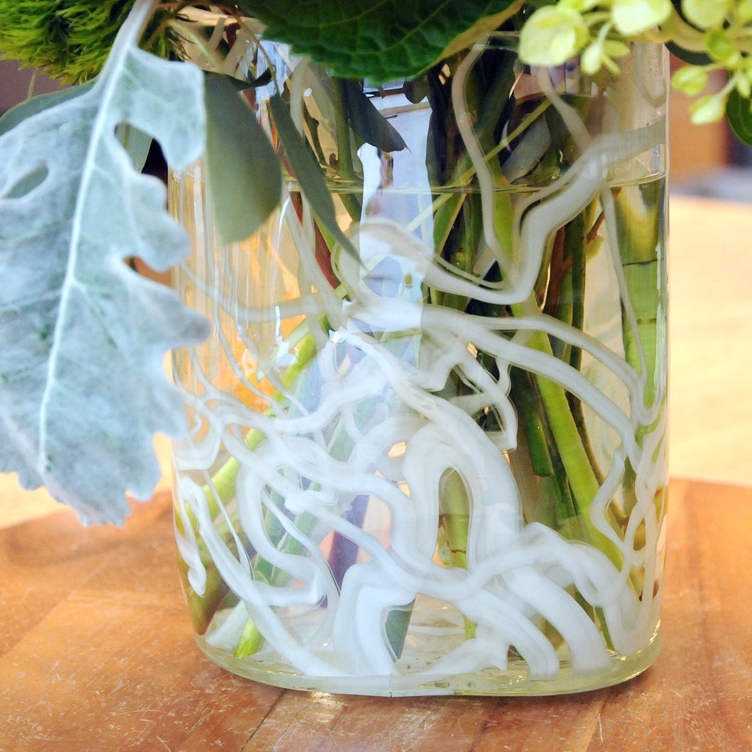 Close up view of tall clear glass vase with white abstract swirl pattern