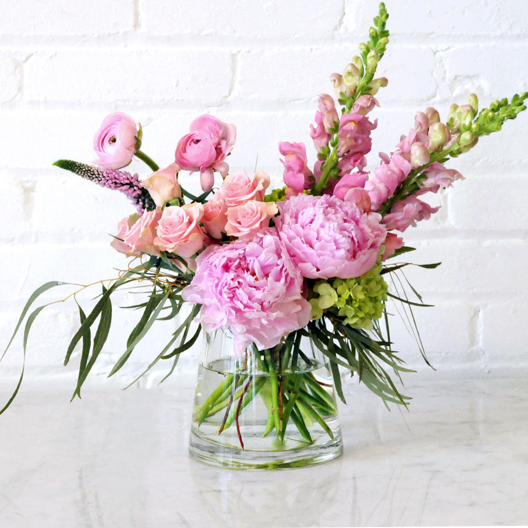 Spruce Flowers Victoria arrangement showing Pink Peonies spray roses and Ranunculus in a clear vase