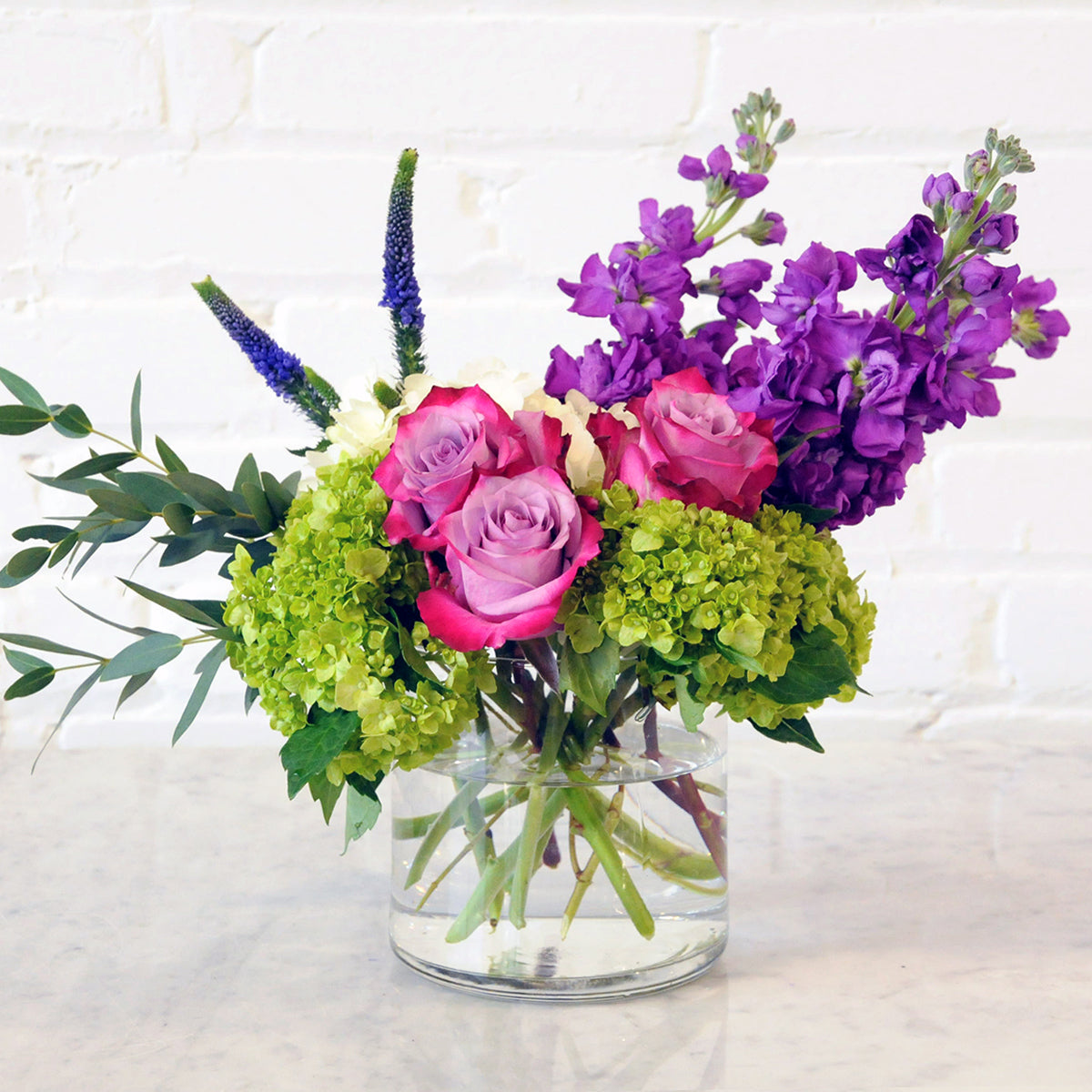 Spruce Flowers York floral arrangement illustrated in a glass vase Deep Purple roses Scent Purple stock set on white Hydrangea 