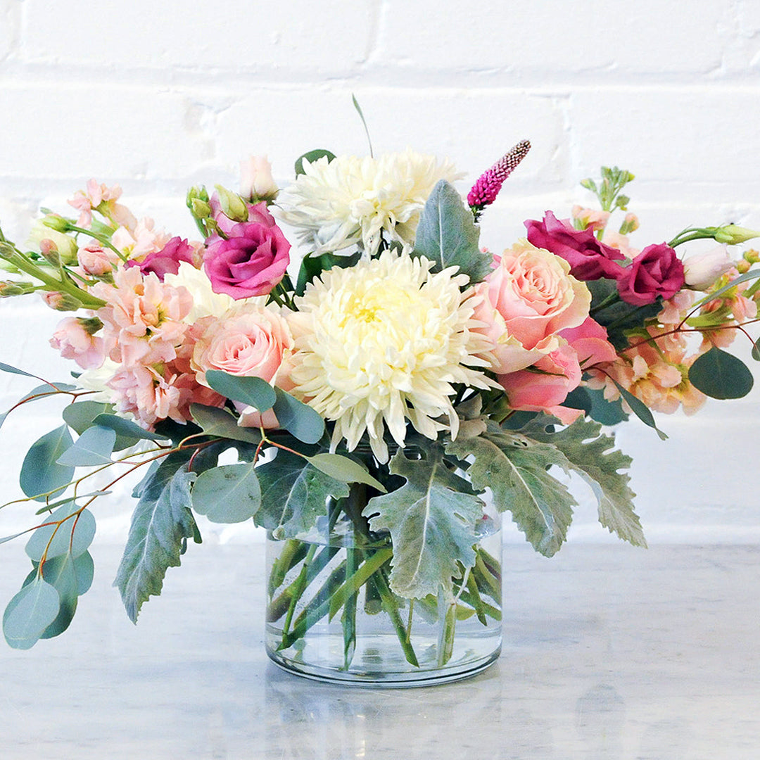 Spruce Flowers Blaisdell arrangement shown in a glass vase with White Chrysanthemums blooms and pink roses and Lisianthus Stock and Veronia.