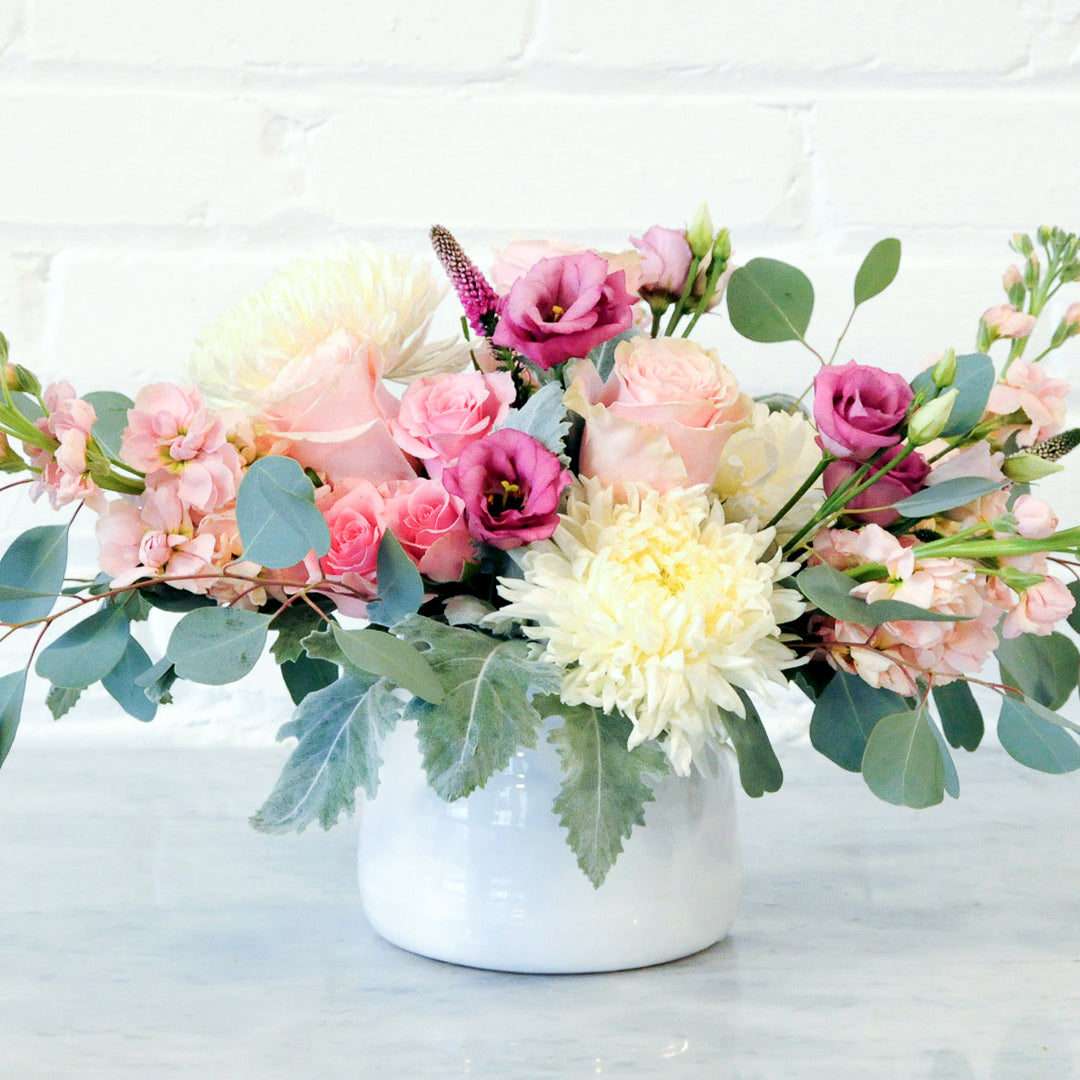 One of our most popular designs, the soft and feminine Blaisdell is full of fragrant pink roses, cinnamon-scented stock and poufs of white standard mums. Available in a glass cylinder or white Tegan ceramic.