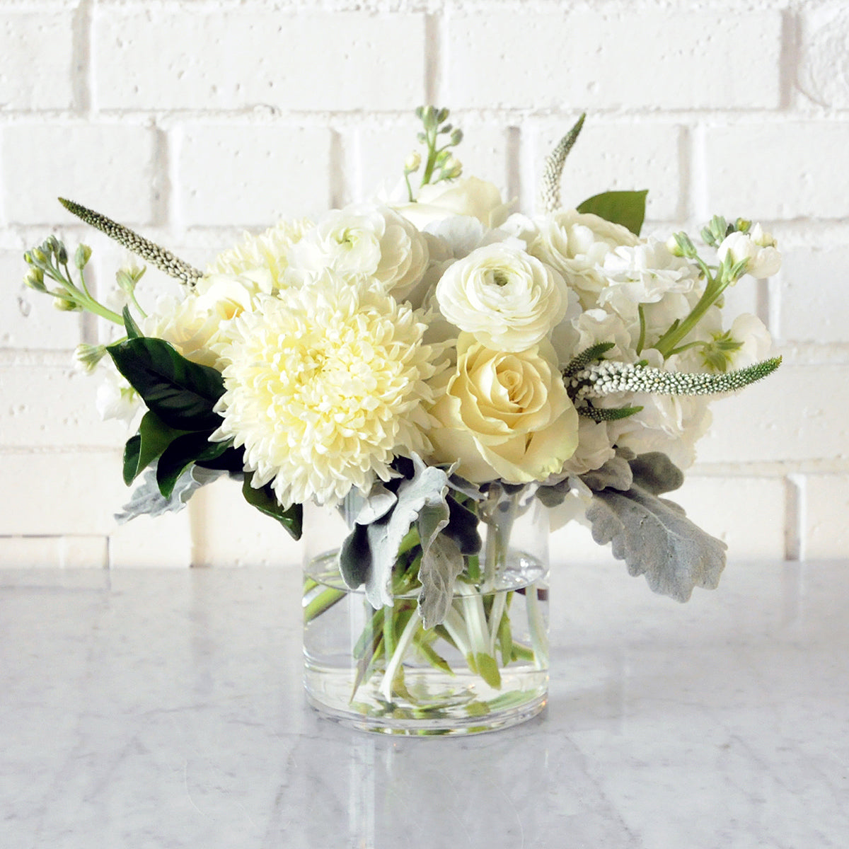 Spruce Flowers como arrangement of white florals shown in a glass vase