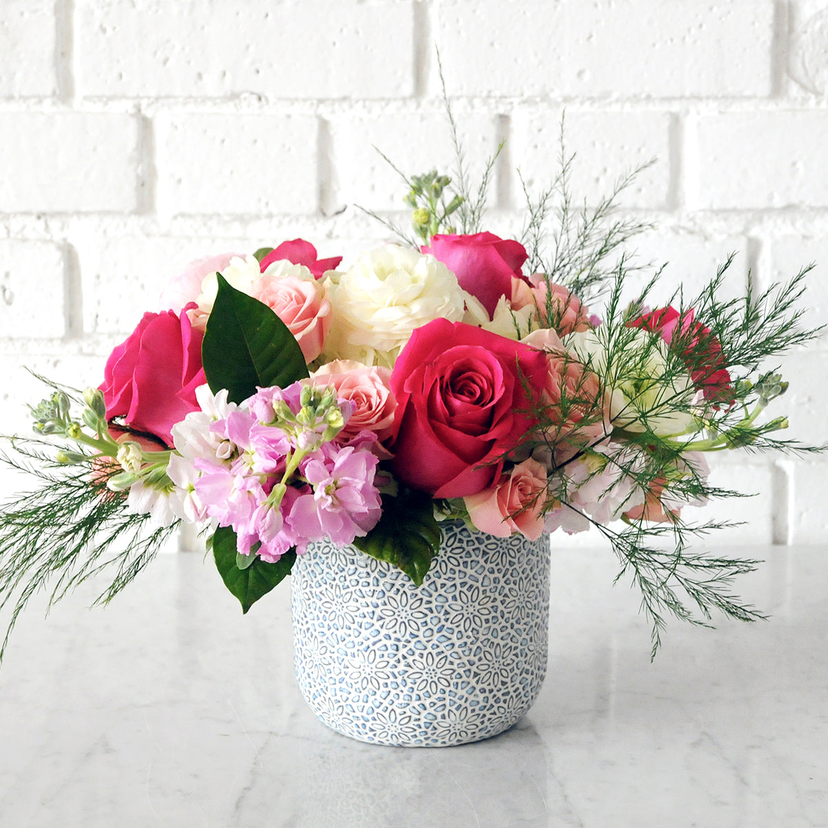 Spruce Flowers Elsie arrangement shown in a blue millie ceramic vase featuring an embossed finish with a blue wash. Florals include Pink Floyd Roses scented stock in pink and whimsical foliage