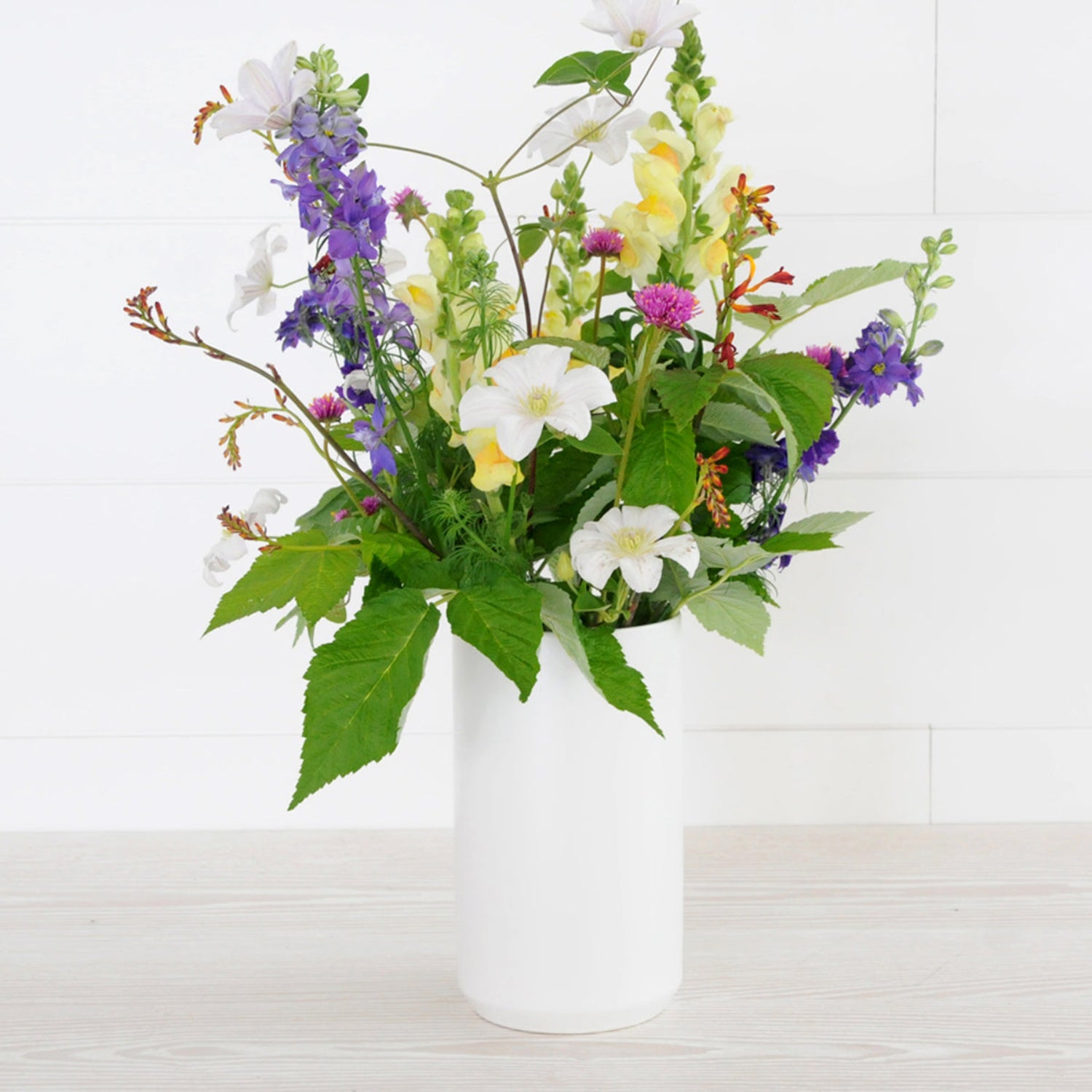 An example of the Larpenteur arrangement featuring delphinium in a tall white ceramic vase