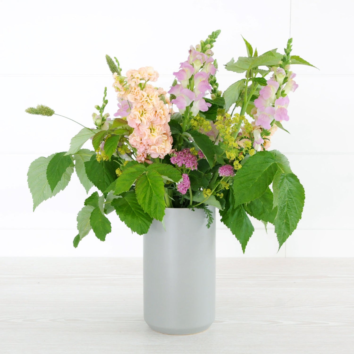 An example of the Larpenteur arrangement featuring yarrow, stock, and snapdragons shown in a tall gray ceramic vase