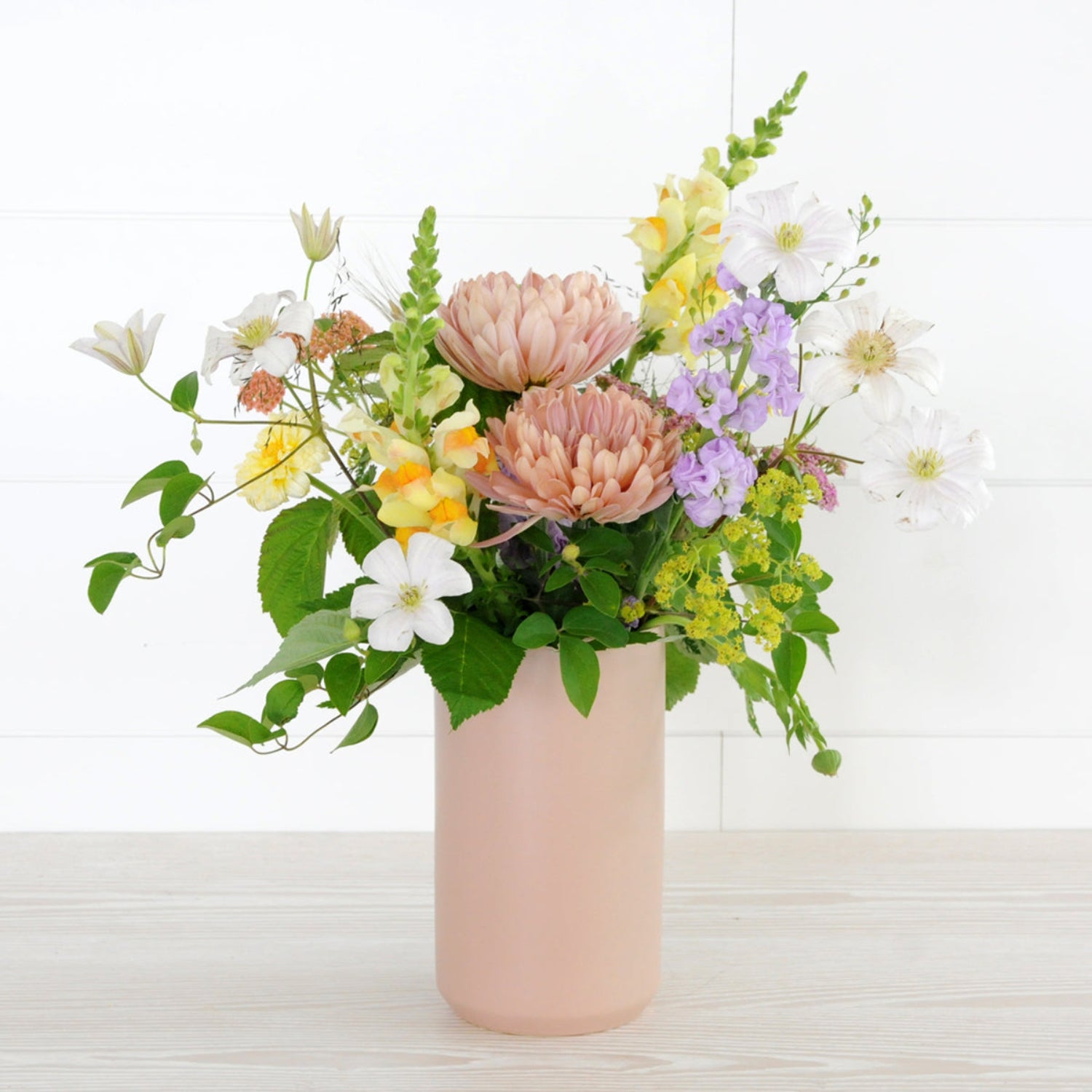 An example of the Larpenteur arrangement featuring chrysanthemums, stock, and snapdragons shown in a tall pastel pink ceramic vase