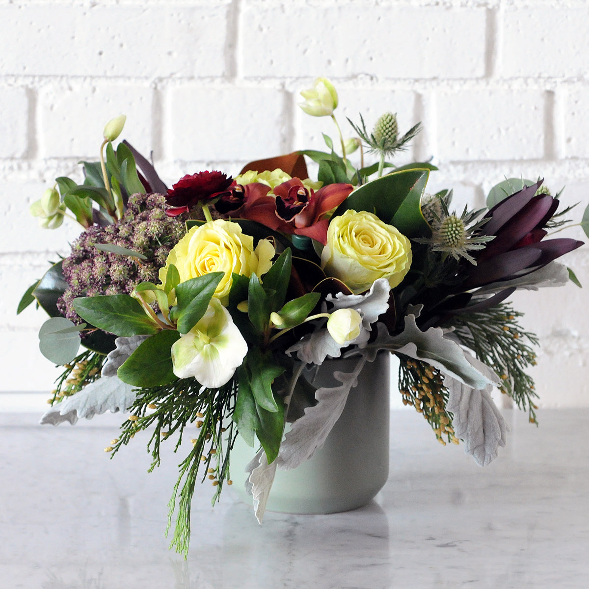 Spruce Winter collection Linden floral arrangement shown in moss green kendal ceramic vase with fresh florals in tones of burgundy, white and featuring chocolate Cymbidium Orchids