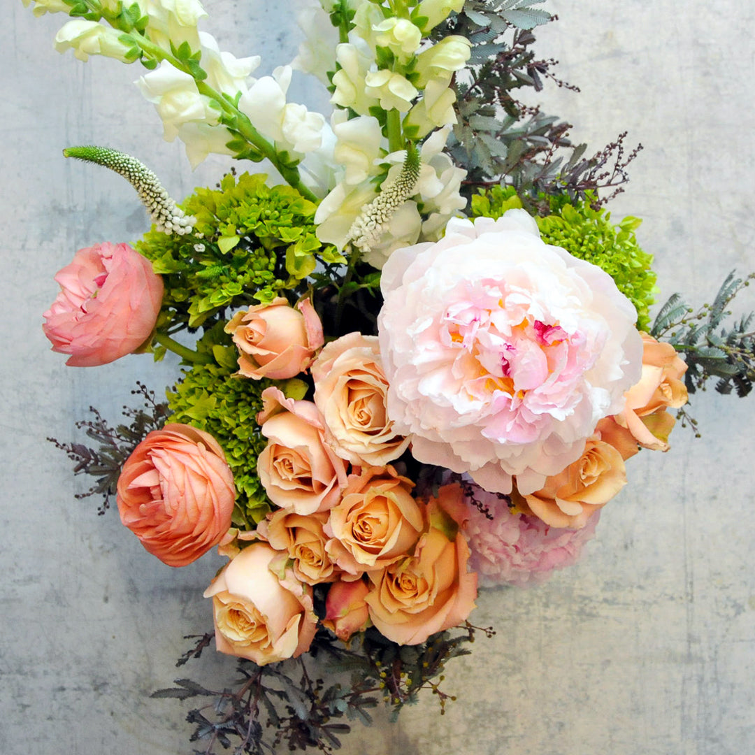 Top down view of Victoria floral Arrangement featuring peonies peach spray roses with Accacia foliage for delivery in Minneapolis and St Paul