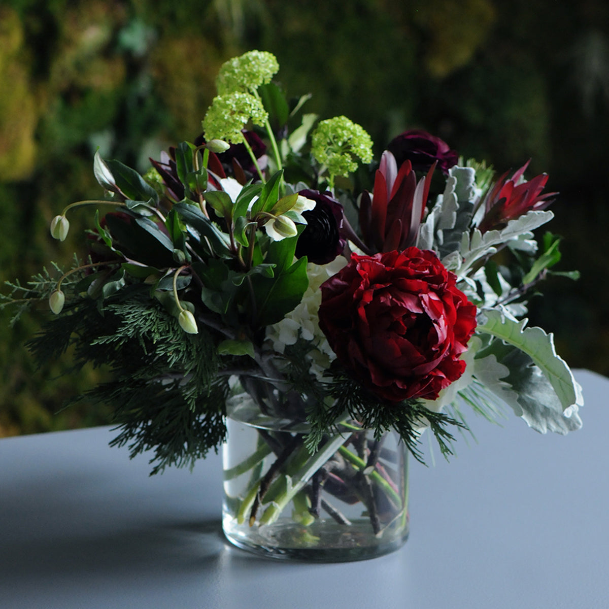Bouquet of red and green flowers in a clear vase on a dark background