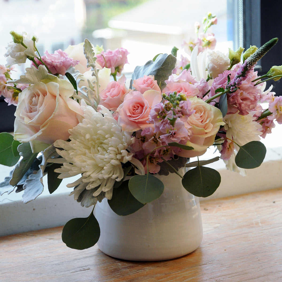 Bouquet of pink and white flowers in a white vase on a wooden surface with a blurred background.