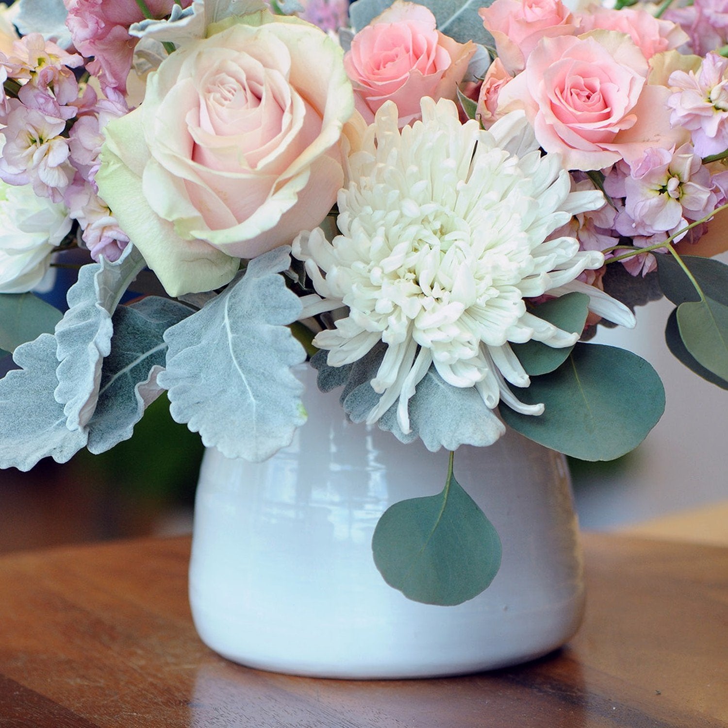 Floral arrangement with pink and white flowers in a white vase on a wooden surface.