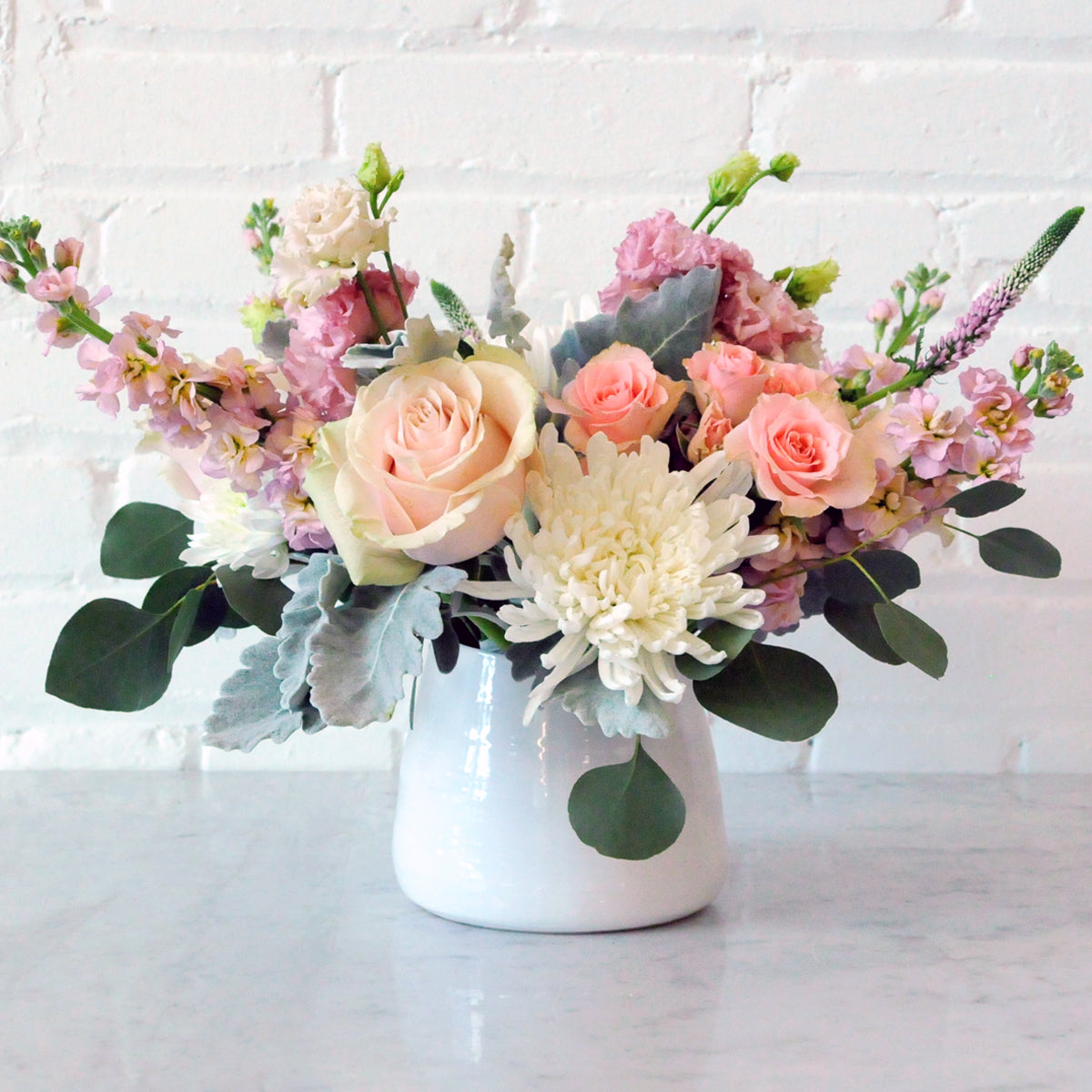 Floral arrangement in a white vase on a light surface with a white brick wall background