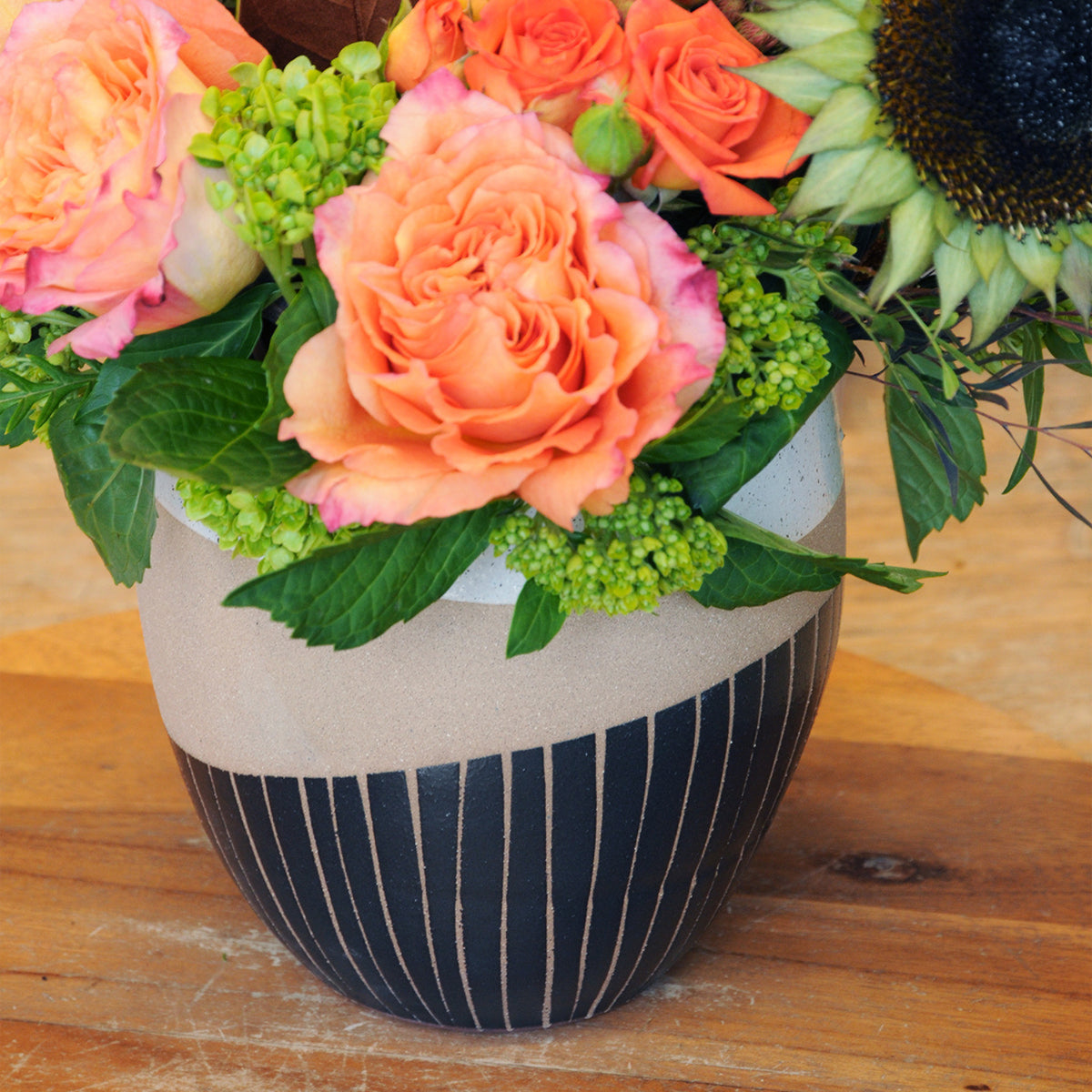 A vibrant autumnal floral arrangement in a ceramic vase with modern White and black detailing, on a wood counter. 