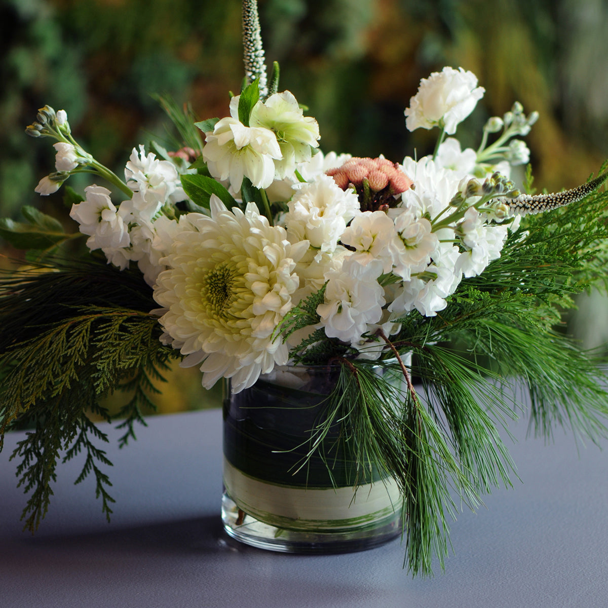Floral arrangement with white flowers and greenery in a glass vase on a reflective surface.