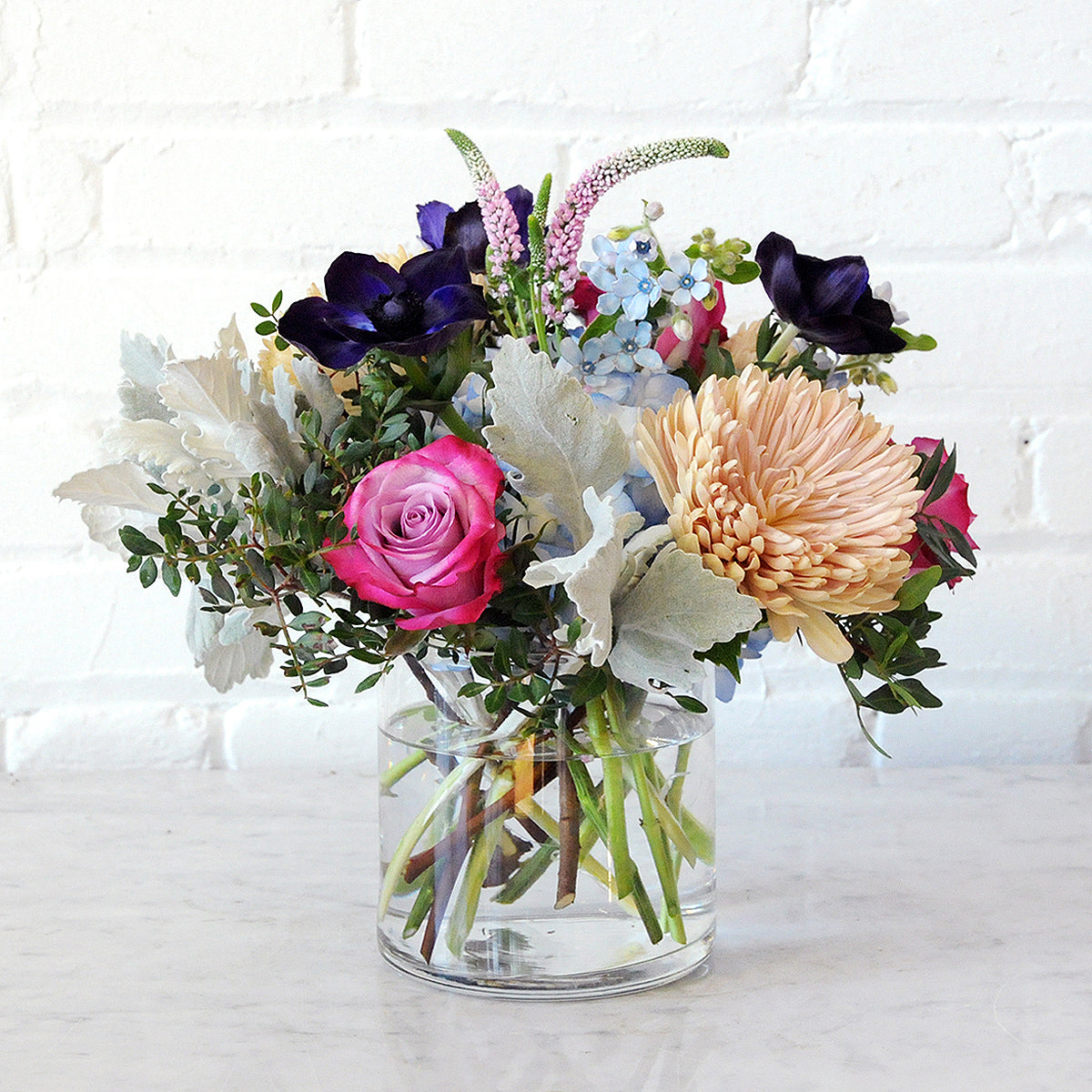 Spruce Flowers Emerson arrangement in a clear glass vase with Blue Hydrangea and dusty miller 