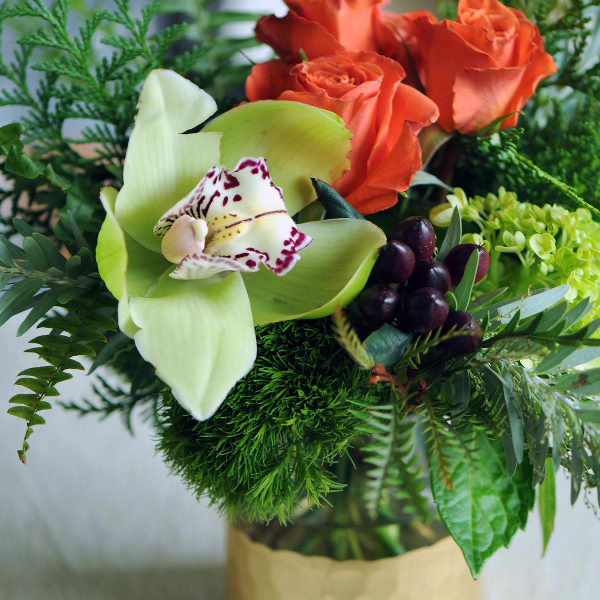 Bouquet of flowers with green orchid, red roses, and greenery in a vase.