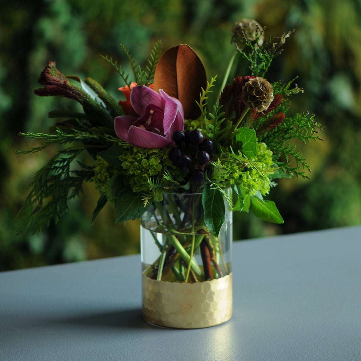 Bouquet of flowers in a clear vase with gold base on a gray surface