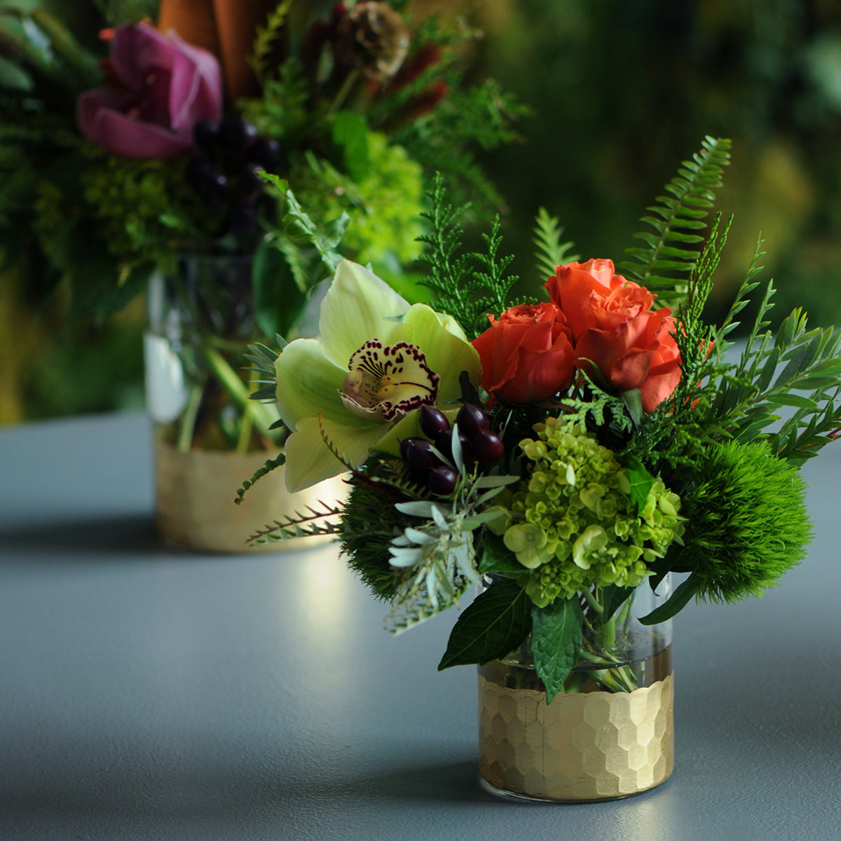 Small bouquet of flowers in a gold vase on a gray surface with blurred background
