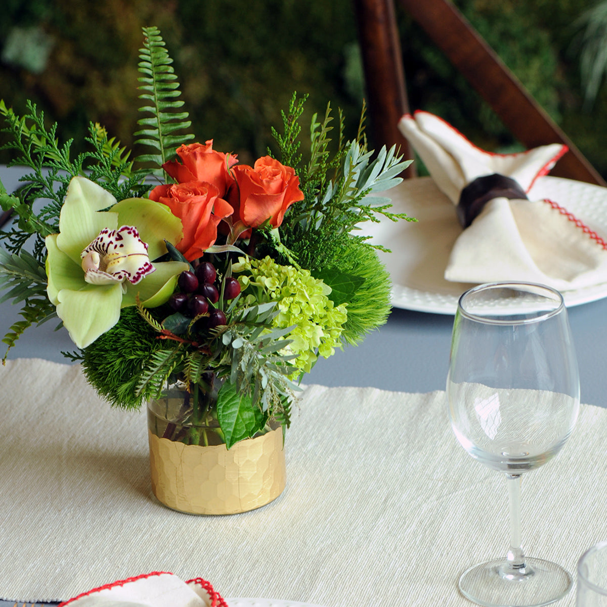 Floral arrangement with red roses and greenery on a table with a glass and napkins.
