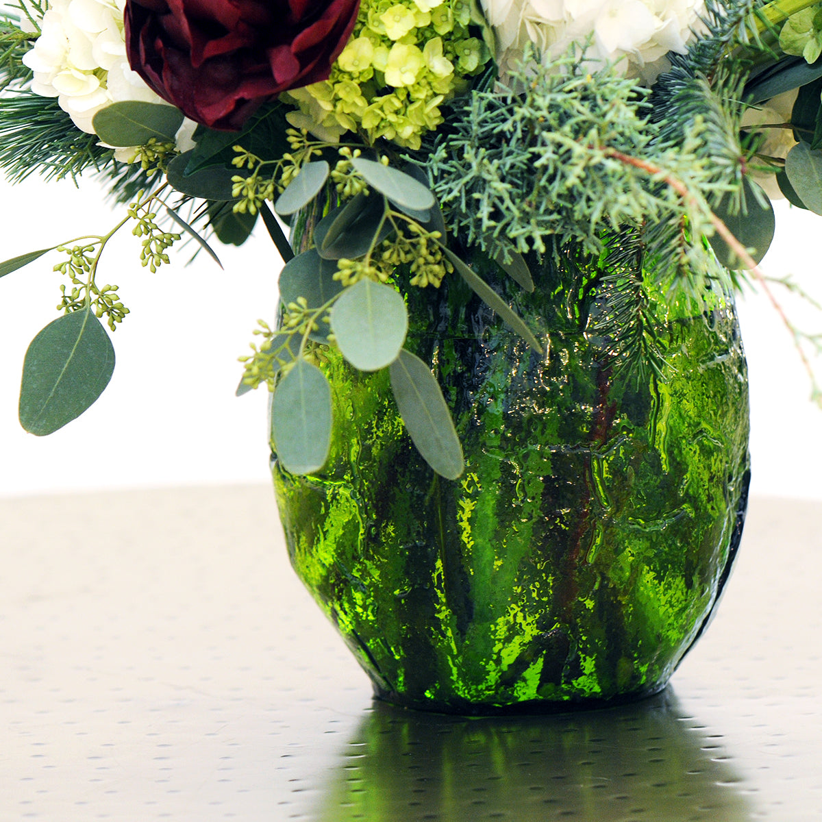 Green textured vase with flowers on a reflective surface