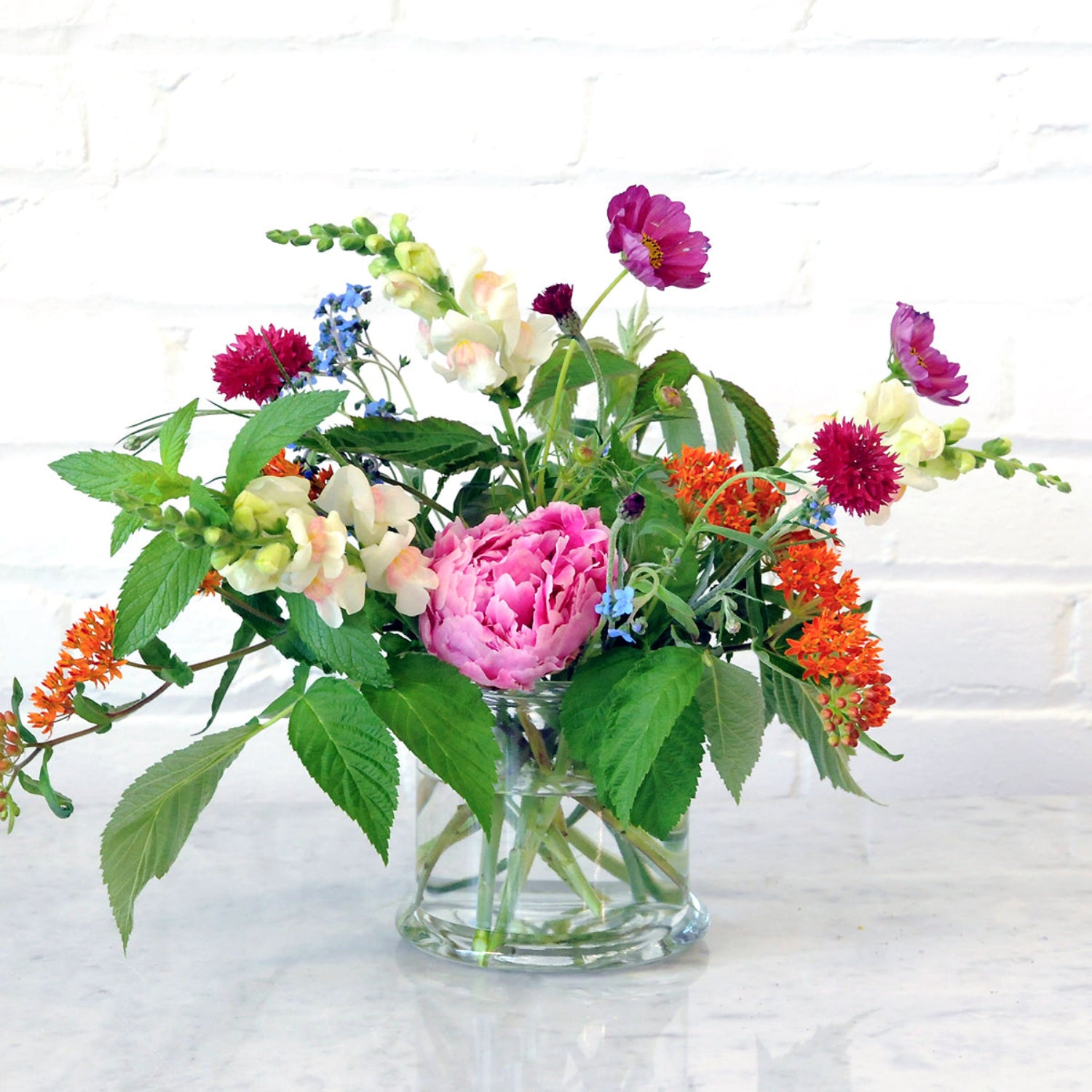 An example of the Larpenteur arrangement featuring peonies and asclepius shown in a glass cylinder