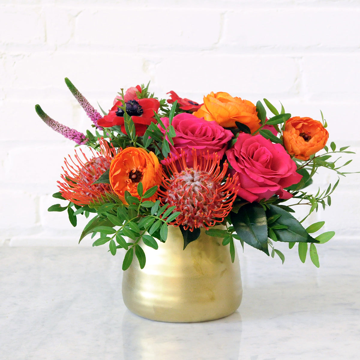 Front photo or a gpld tegan ceramic vase with Spruce Flowers Lexington Arrangement featuring Pink Floyd roses and orange Ranunculus.  