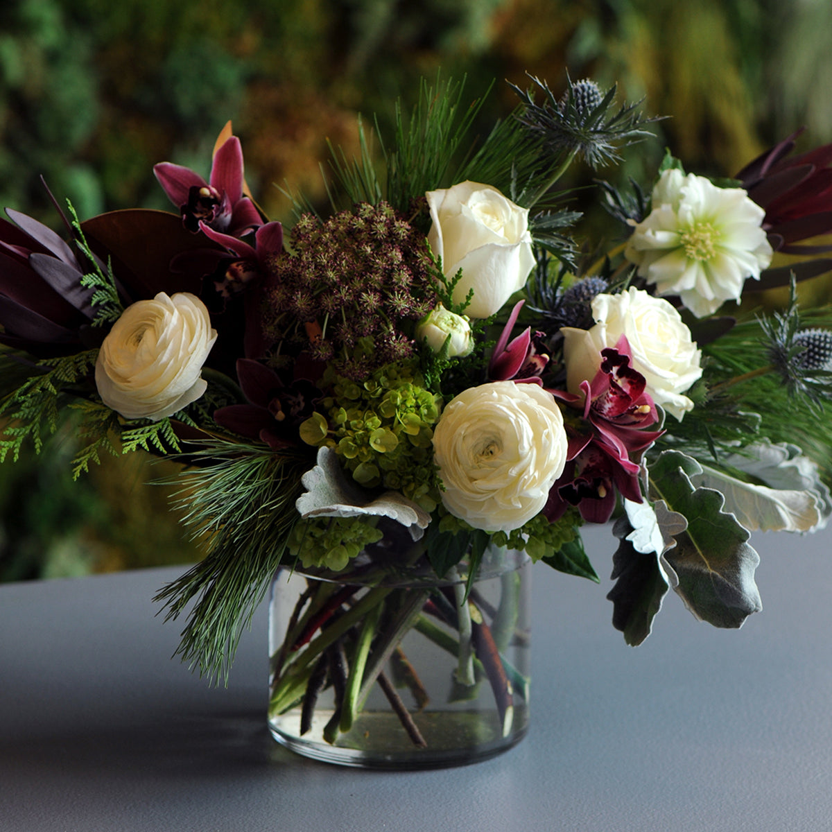 Bouquet of flowers in a clear vase on a dark surface with a blurred green background